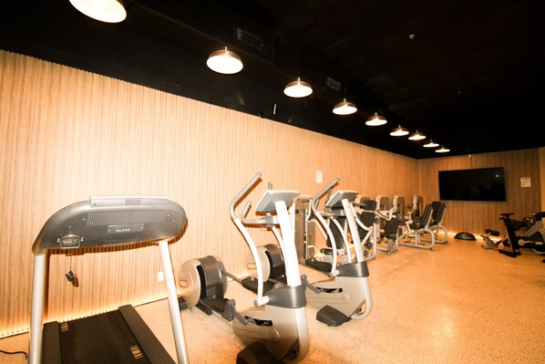 Une salle de sport avec des tapis de course et des vélos d’appartement disposés en rangées.
