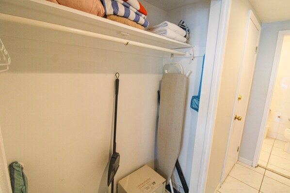 A laundry room with a shelf holding folded towels and a box on the floor.