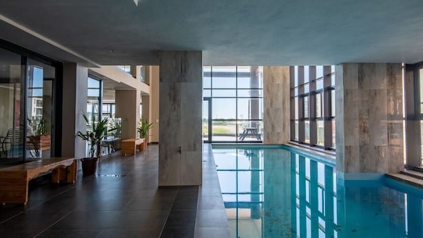 A spacious indoor swimming pool area with large windows, a wooden bench, and potted plants. - Cute and Cosy Studio Marina 501 (uMhlanga Ridge, KwaZulu-Natal)