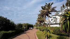A paved pathway lined with palm trees and greenery, leading towards a modern building with multiple balconies. - Cute and Cosy Studio Marina 501 (uMhlanga Ridge, KwaZulu-Natal)