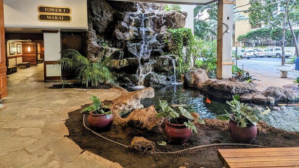 A hotel lobby with a waterfall feature, potted plants, and a sign indicating 'Tower I Makai'. - Part Ocean View, Beach Theme 23rd Fl, Free Parking with WiFi, AC  (Honolulu)