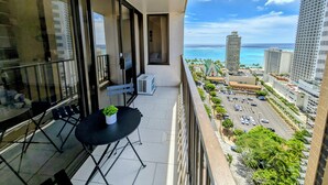 A balcony with a table and chairs, a potted plant, and a view of the ocean and cityscape. - Part Ocean View, Beach Theme 23rd Fl, Free Parking with WiFi, AC  (Honolulu)