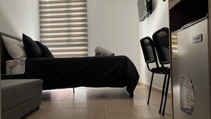 Moderni, pelkistetty huone, jossa on sänky, sohva, ruokapöytä ja jääkaappi.