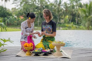 Dos personas realizando un ritual junto a una piscina, con diversas ofrendas y un tapete tejido.