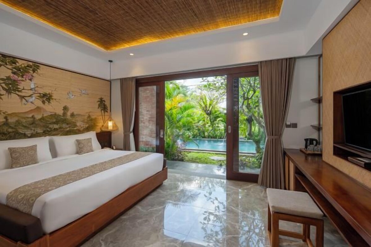 Un dormitorio con una cama grande, televisión y vistas a una piscina y vegetación.
