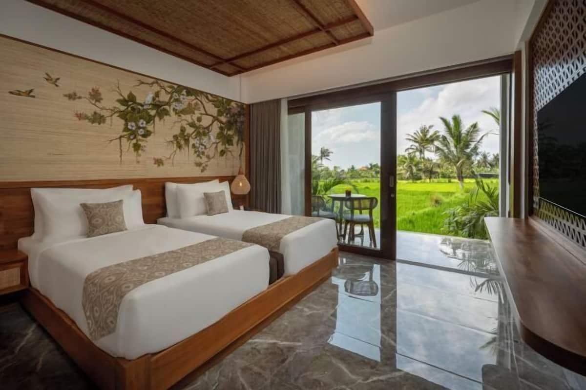 A hotel room with two beds, a large window, a dining area, and a view of a green landscape.