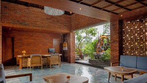 A spacious lobby with a brick wall, wooden furniture, and a seating area with a view of greenery outside. - Emana Akatara (Ubud)