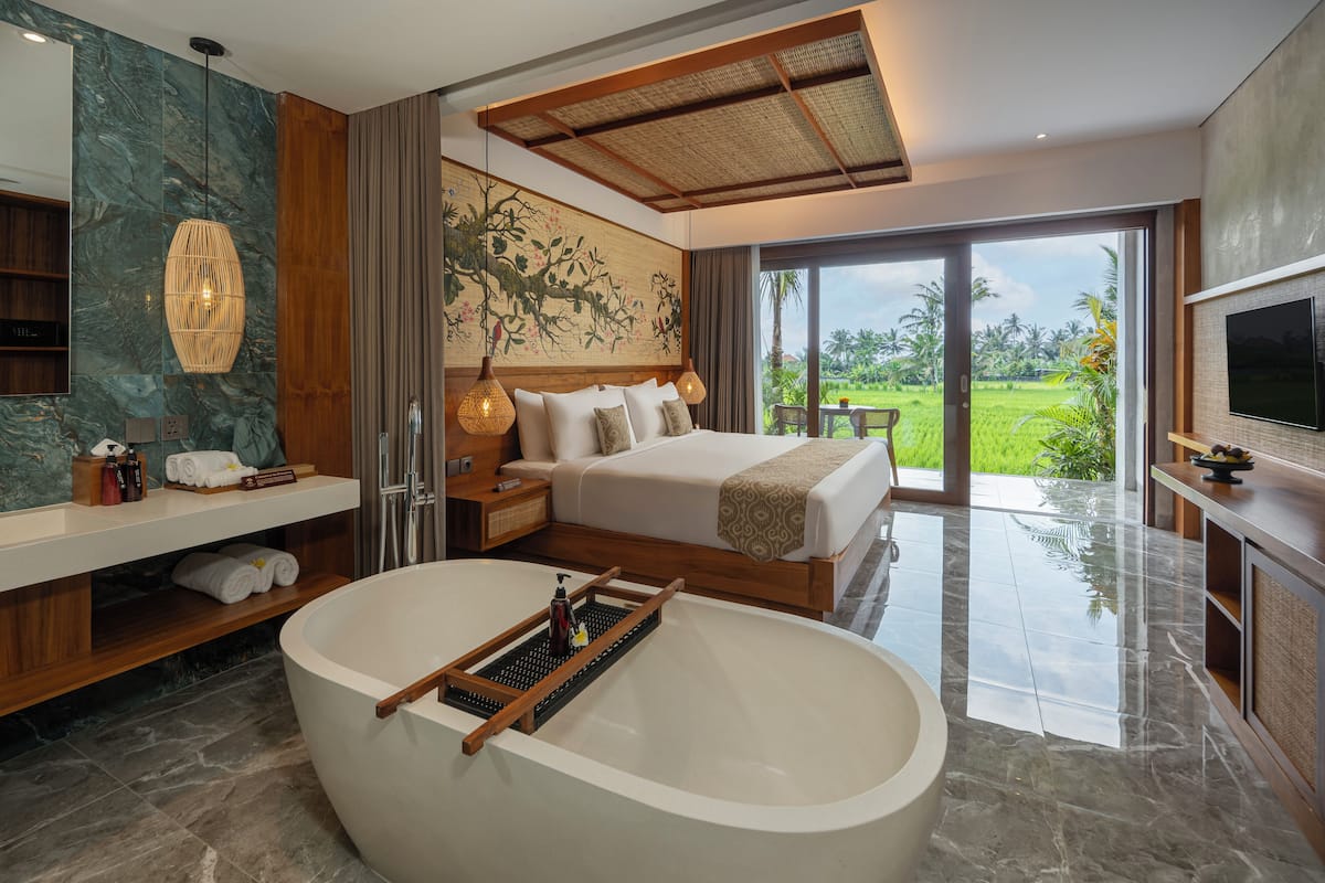 A modern bedroom with a large bed, a bathtub, and a view of a lush garden.