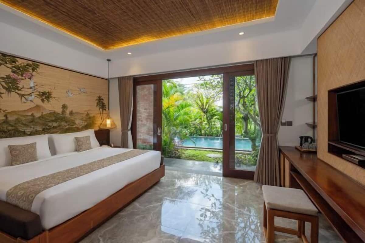 A bedroom with a large bed, a TV, and a view of a pool and greenery.