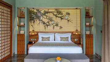 A modern hotel room with a large bed, a round table with a flower centerpiece, and a traditional-style wall hanging.
