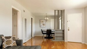 A spacious living area with a wooden floor, a dining table with chairs, a sofa with patterned cushions, and a staircase leading to an upper level.