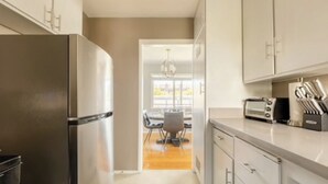 A modern kitchen with stainless steel appliances, a dining area with a chandelier, and light-colored cabinetry.