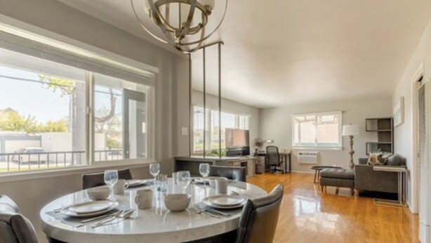 A modern dining area with a round table set for four, large windows, and a kitchen in the background.
