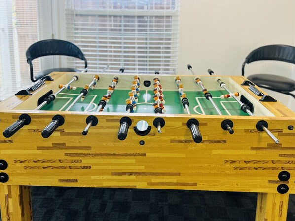 A wooden foosball table with a green playing surface and black and white goalposts.