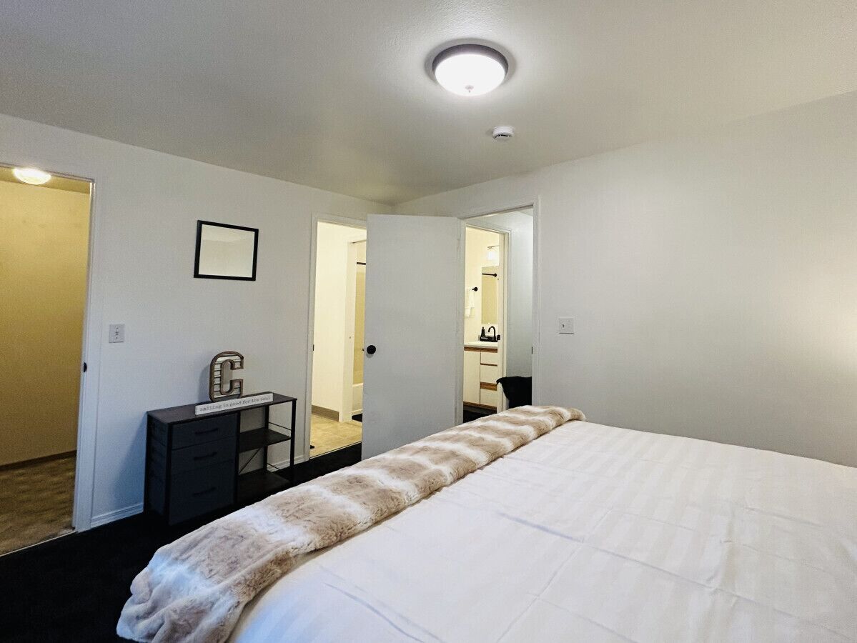 A hotel room with a large bed, a desk with a chair, a small cabinet, and a mirror on the wall.