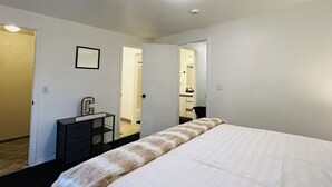 Habitación de hotel con una cama grande, un escritorio con silla, un armario pequeño y un espejo en la pared.