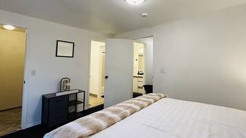 A hotel room with a large bed, a desk with a chair, a small cabinet, and a mirror on the wall.