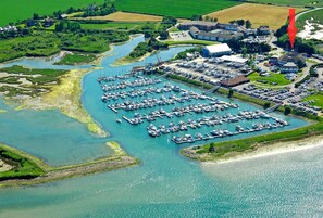 An aerial view of a marina with numerous boats docked, surrounded by green fields and a small body of water.