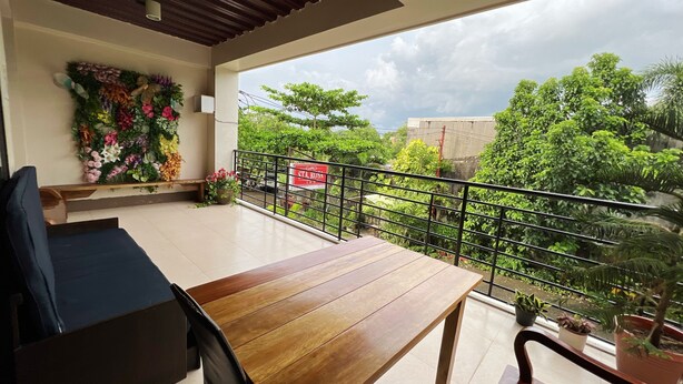 Un balcon avec une table et des chaises en bois, une décoration murale florale et une vue sur la verdure et les bâtiments.