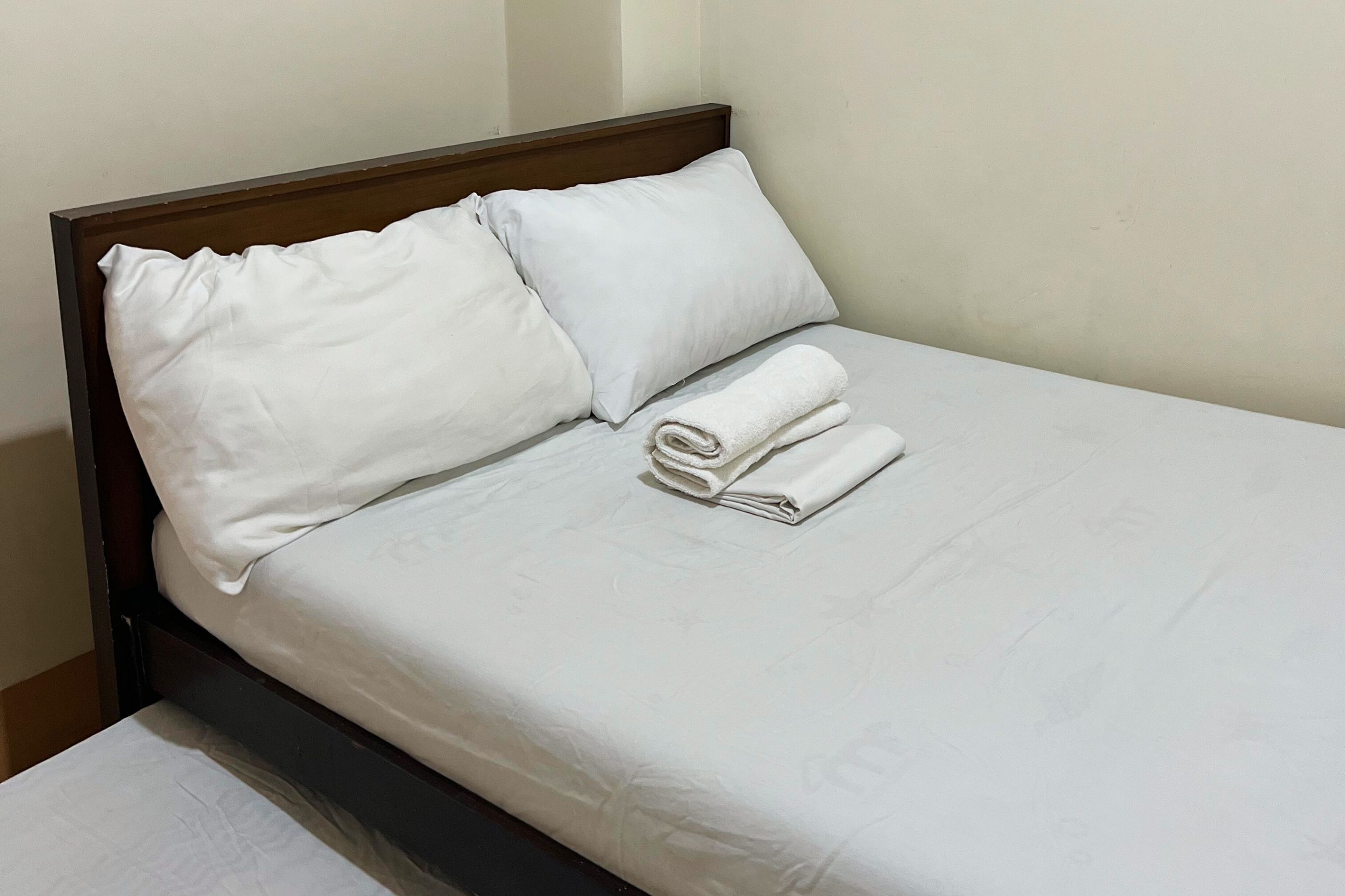 Een netjes opgemaakt bed met witte lakens en kussens, een opgevouwen handdoek op het bed, en een houten hoofdbord.