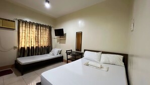Une chambre d’hôtel avec deux lits simples, un bureau, une chaise, une télévision et une fenêtre avec des rideaux.