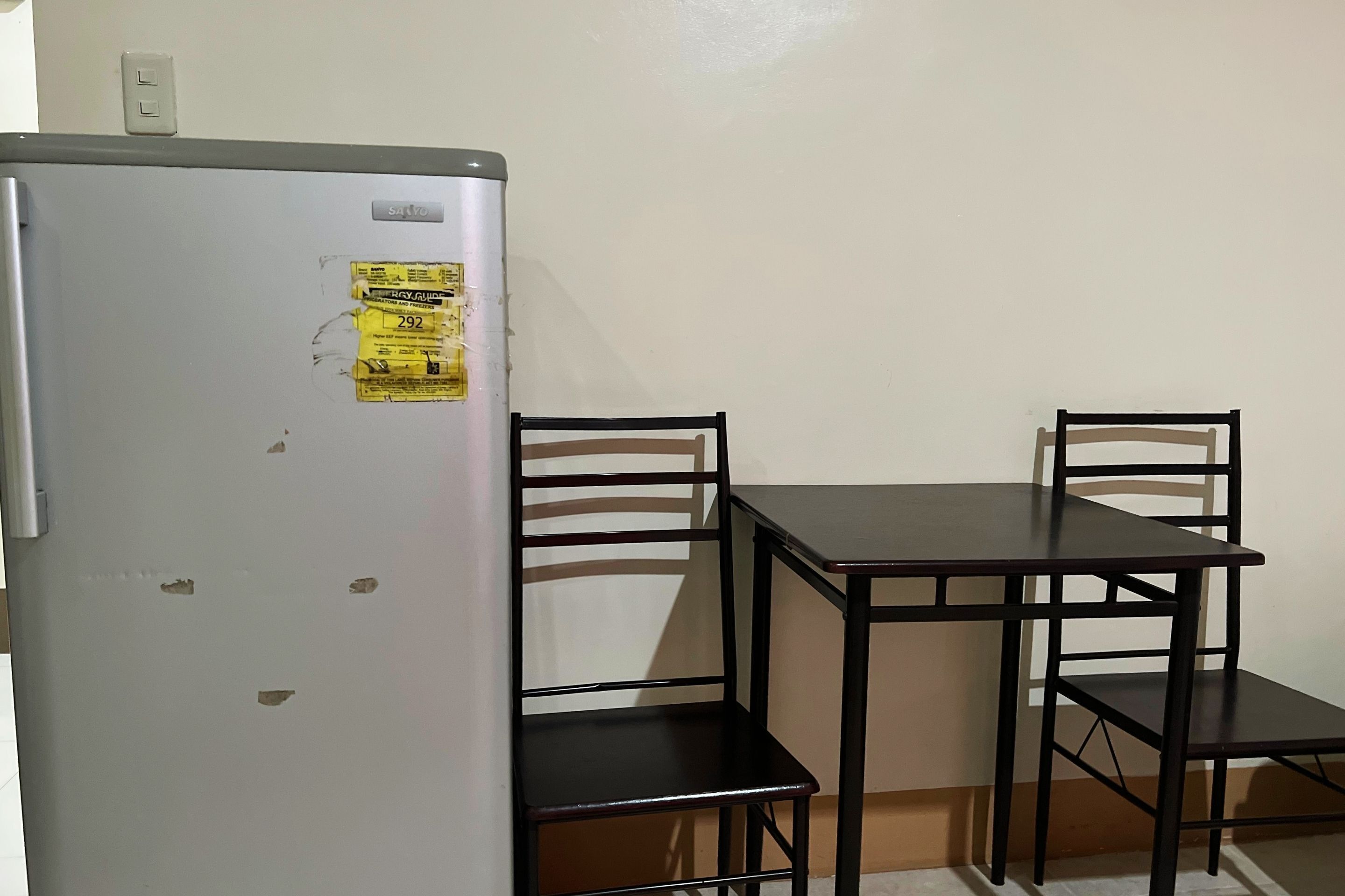 A small room with a white refrigerator, two wooden chairs, and a dark wooden table.