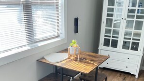 Een eethoek met een houten tafel en banken, een wit kastje met glazen deuren, en een raam met zonwering.