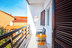 Ein Balkon mit Geländer, ein kleiner Tisch mit Pflanze und ein Fenster mit Fensterläden.