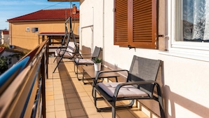 Un balcon avec des sièges d’extérieur, une balustrade et une vue sur un immeuble dont le toit est rouge.