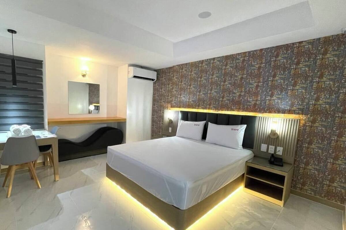 A modern hotel room with a large bed, bedside tables, a desk, and a chair.