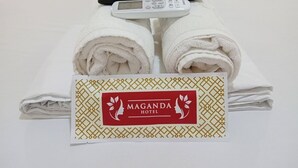 A neatly made bed with rolled white towels, a remote control, and a sign for Maganda Hotel. - Maganda Hotel-San Fernando (Bacolor)