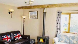Un salon avec une cheminée, un canapé orné de drapeaux britanniques, une lampe et une fenêtre avec des rideaux.