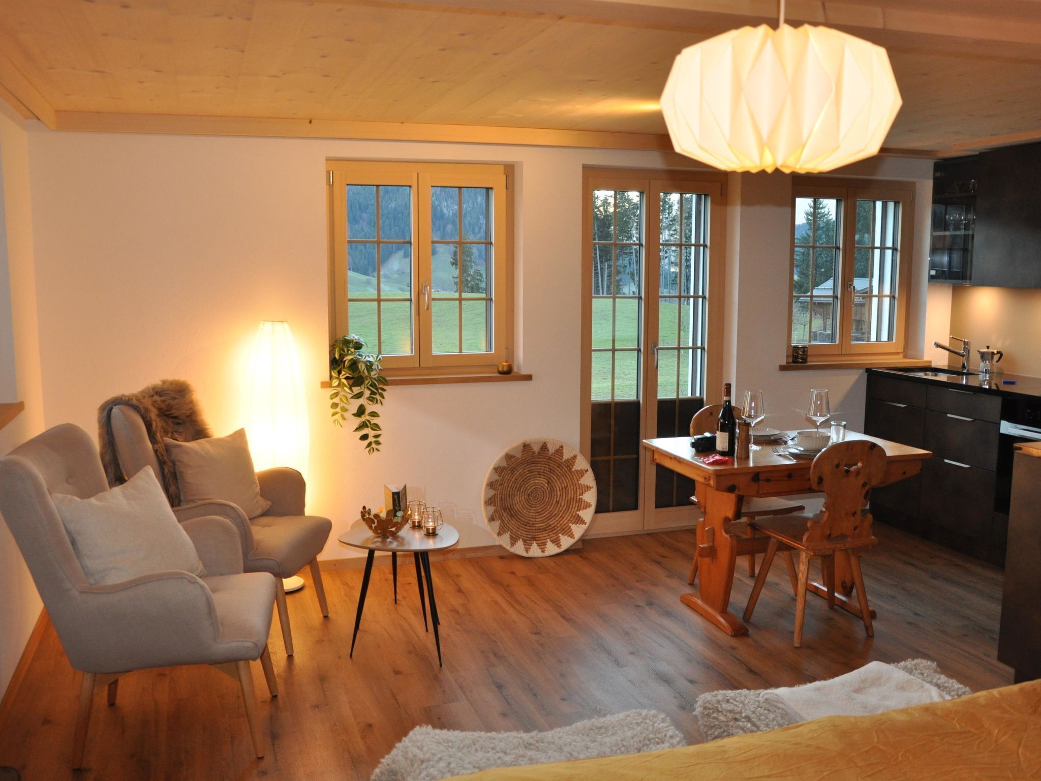 Ein gemütliches Wohnzimmer mit einer Couch, einem Esstisch und einer Küchenzeile mit Holfschränken und einer Hängelampe.