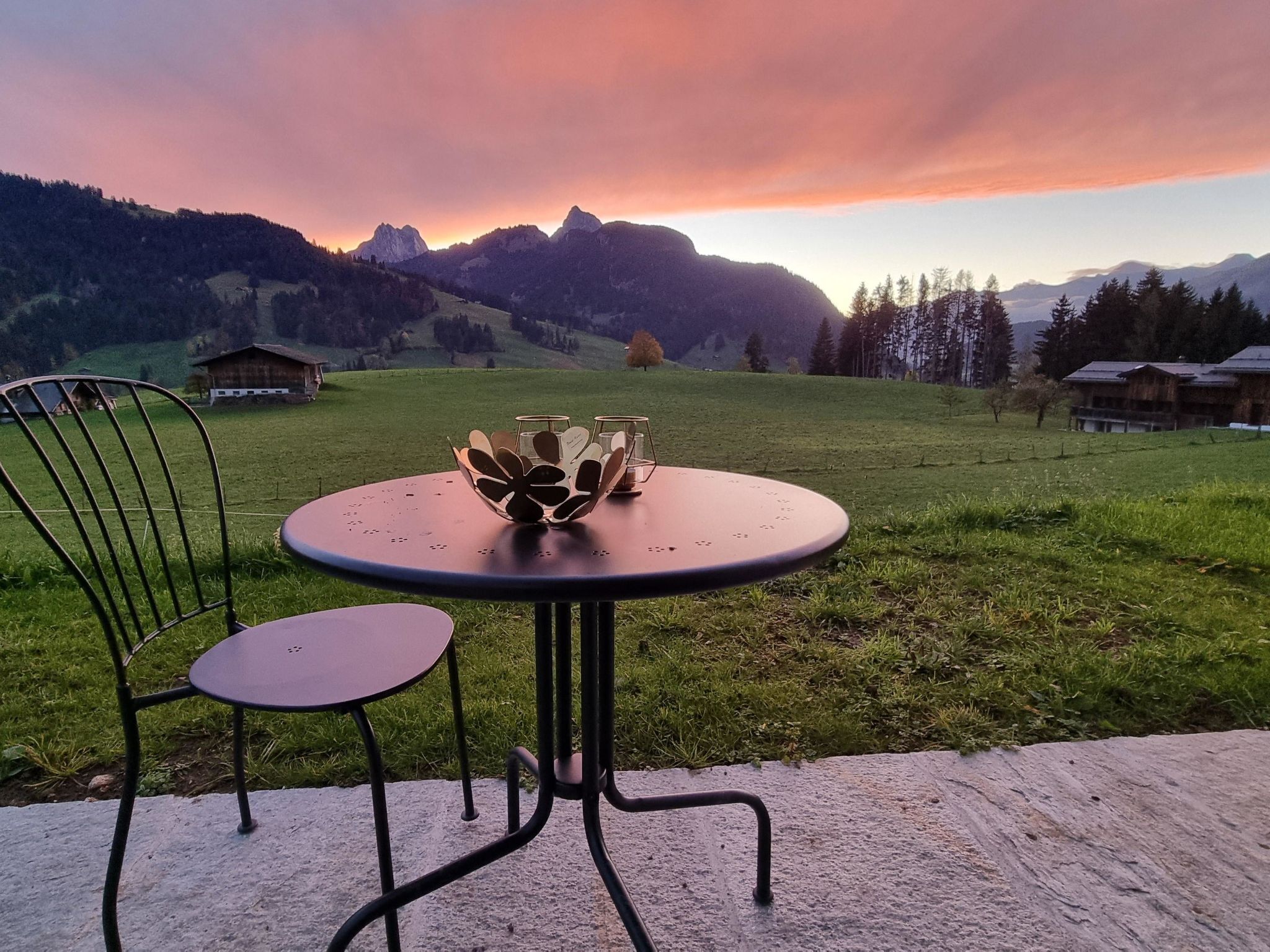 Ein Tisch mit Stühlen im Freien mit Blick auf Berge und einen Sonnenuntergang.