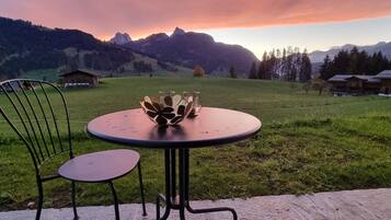 Ein Tisch mit Stühlen im Freien mit Blick auf Berge und einen Sonnenuntergang.