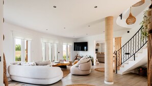 A spacious living area with a curved white sofa, a round coffee table, and a large TV mounted on the wall. - Kistine 5 bedroom villa, Cala Morell (Cala Morell)