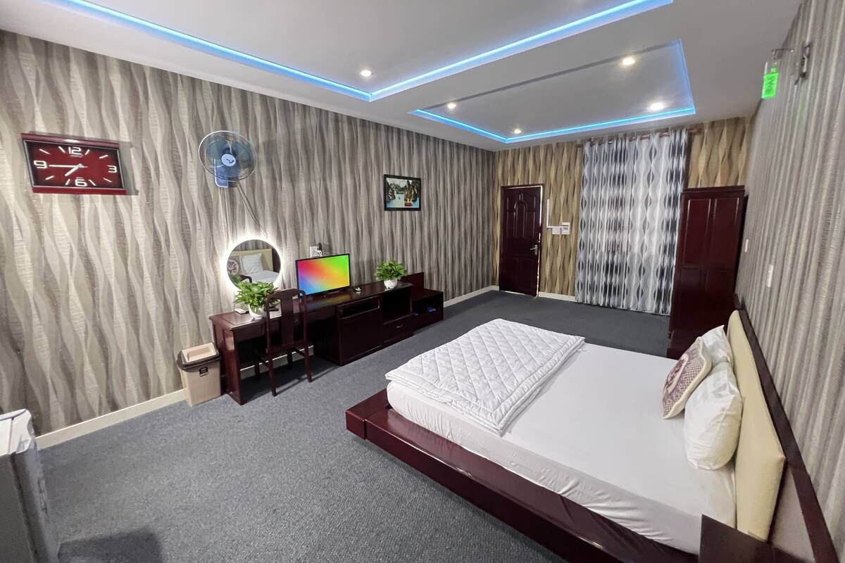 A modern bedroom with a large bed, a desk, a computer, and a clock on the wall.
