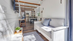 A compact living space with a sofa, a small kitchen area, and a dining table. - New - Pine View MicroCabin - Rare (Broken Bow)
