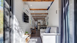 A modern interior with a wooden ceiling, white walls, and a kitchen area visible in the background. - New - Pine View MicroCabin - Rare (Broken Bow)