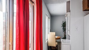 Un couloir étroit avec un coin repas comprenant une table ronde et une chaise, une plante en pot et un mur blanc avec un interrupteur.