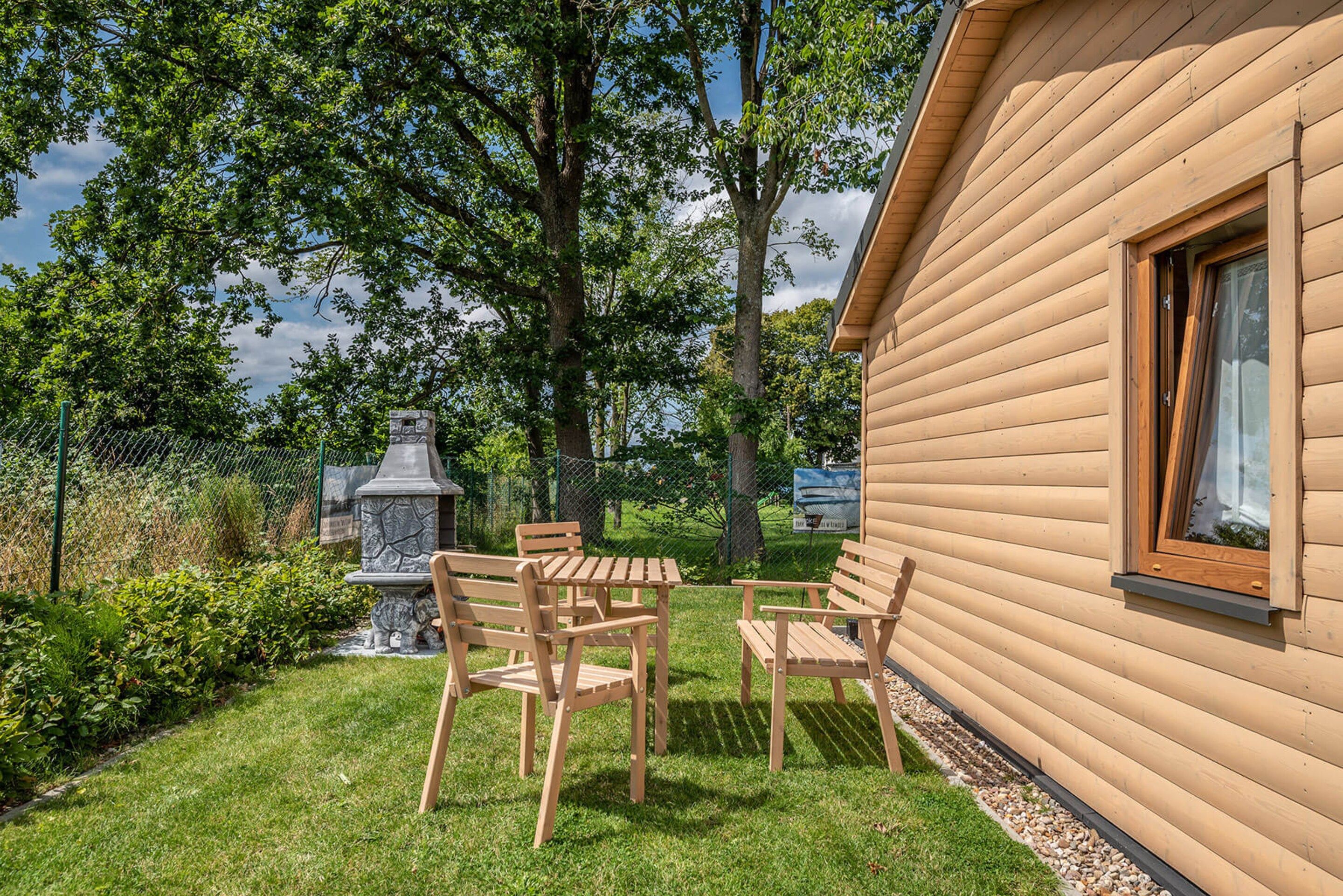 A wooden cabin with a stone fireplace, a table and chairs, and a garden with a fence and trees.