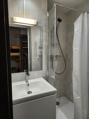A bathroom with a glass-enclosed shower, a white sink, and a mirror above it. - 4-person studio near the slopes (Les Deux Alpes)