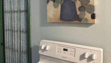 Een keuken met een witte Crosley-oven, een groene deur en een schilderij van een vaas met bladeren aan de muur.