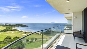 A balcony with a glass railing overlooking a golf course and beach.