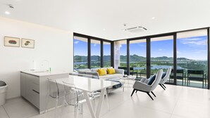 A modern kitchen with a white countertop, clear chairs, and a view of a lake and mountains through large windows.