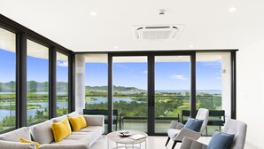 A modern living room with a large sliding glass door leading to a balcony with a scenic view of a lake and mountains.