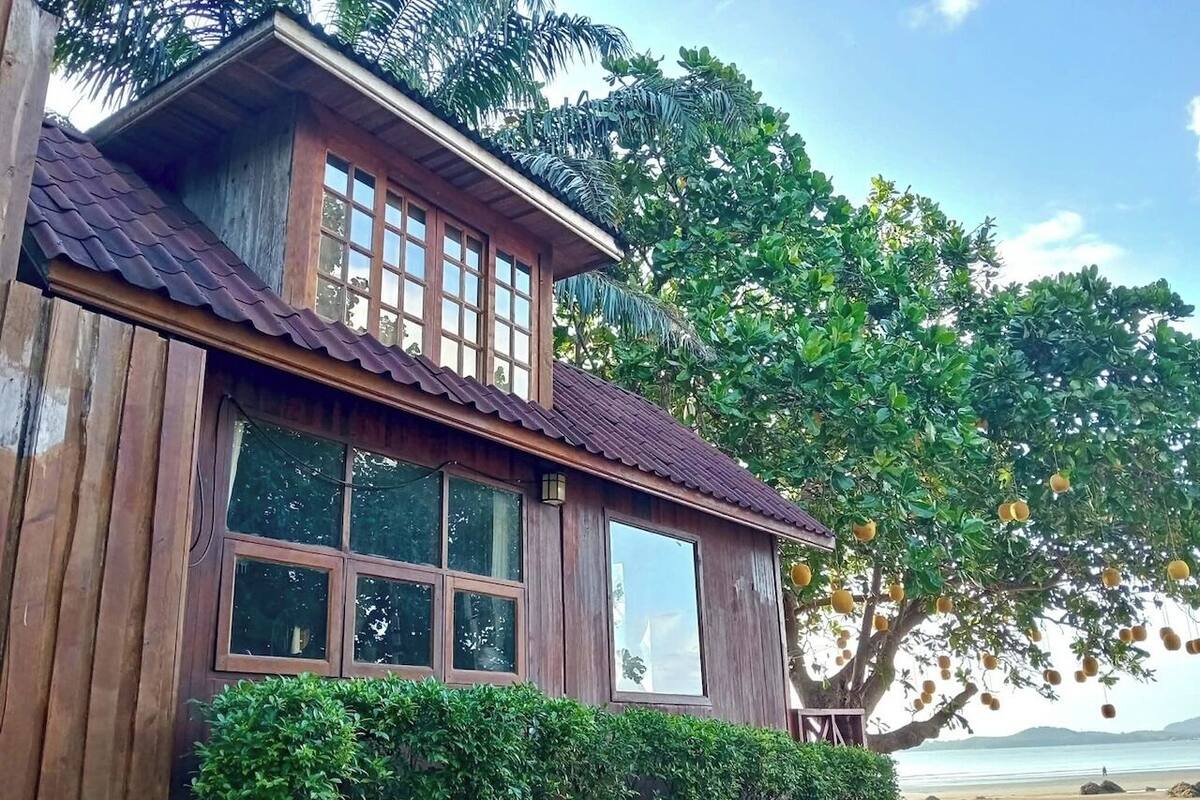 A wooden house with a tiled roof, large windows, and a view of the beach.