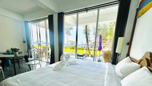 A hotel room with a large bed, a desk with a chair, and a view of a garden and beach through large windows. - 7 Heaven camping Lanta (Ko Lanta)