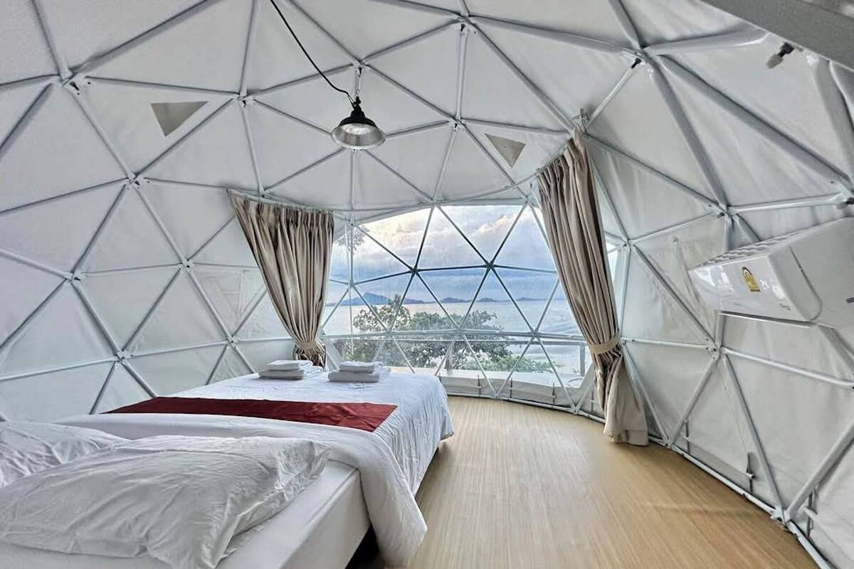 A dome-shaped room with a bed, curtains, and a view through a large window.