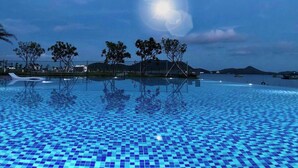 Una piscina con suelo de baldosas, rodeada de árboles y vistas al mar.